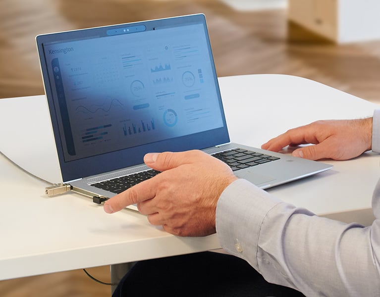 Man about to put his finger on his Vermiark device to unlock his laptop secured with a Kensington lock, verimark fingerprint security key and privacy screen, protecting data from threats.