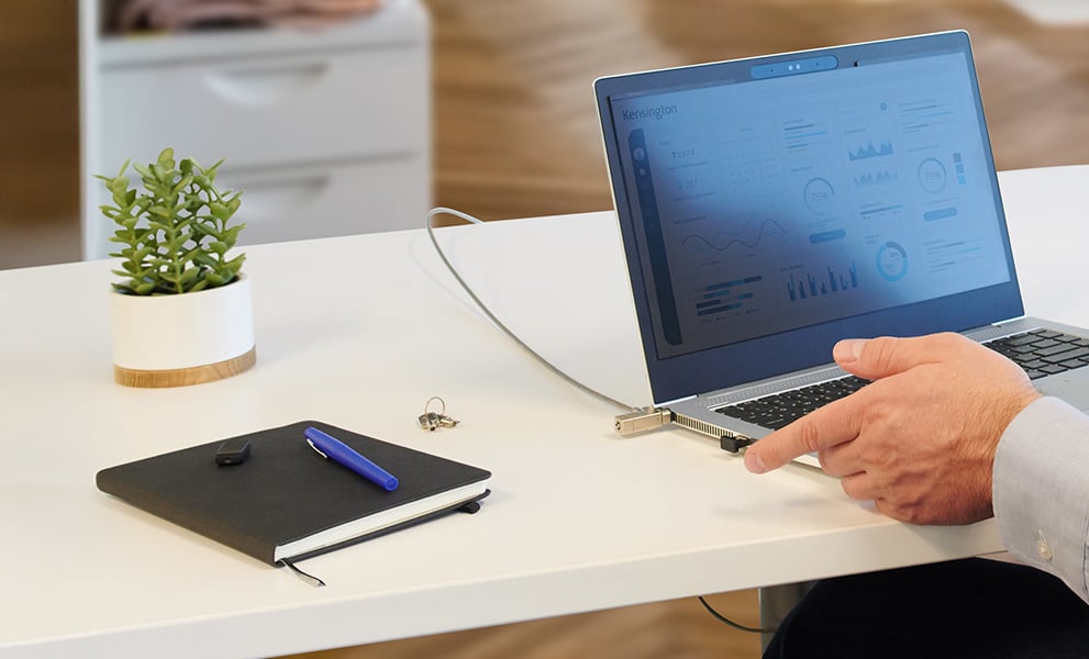 Man about to put his finger on his Vermiark device to unlock his laptop secured with a Kensington lock, verimark fingerprint security key and privacy screen, protecting data from threats.